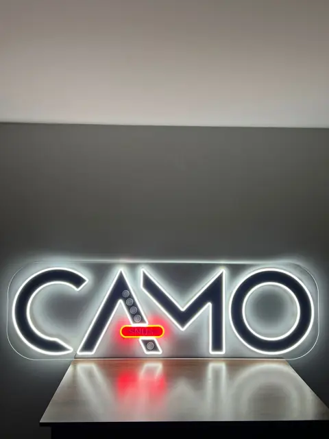 Baltas LED neoninis logotipas su raudonu akcentu ant stovo