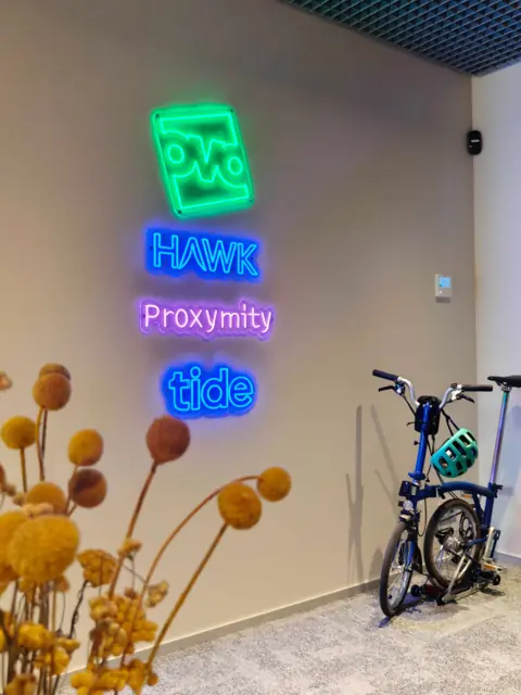 Trys skirtingų spalvų LED neoniniai logotipai vienoje biuro sienoje