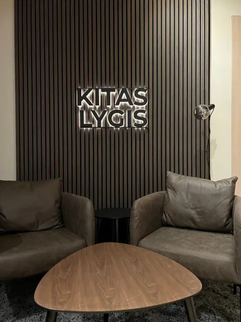 Baltos LED tūrinės raidės ant medinių lamelių sienos poilsio zonoje